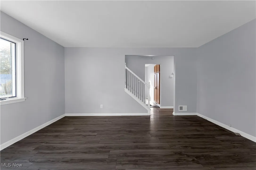 Unfurnished room featuring dark wood-type flooring and stairs