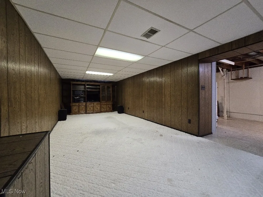 Finished Lower Level with wood paneled walls, light carpet, and a drop ceiling.