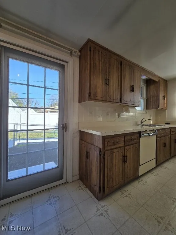 Kitchen featuring light countertops, tasteful backsplash, dishwasher, and brown cabinets.