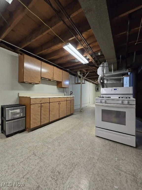 Kitchen with light countertops, (extra) white gas stove, light flooring, and brown cabinets.
