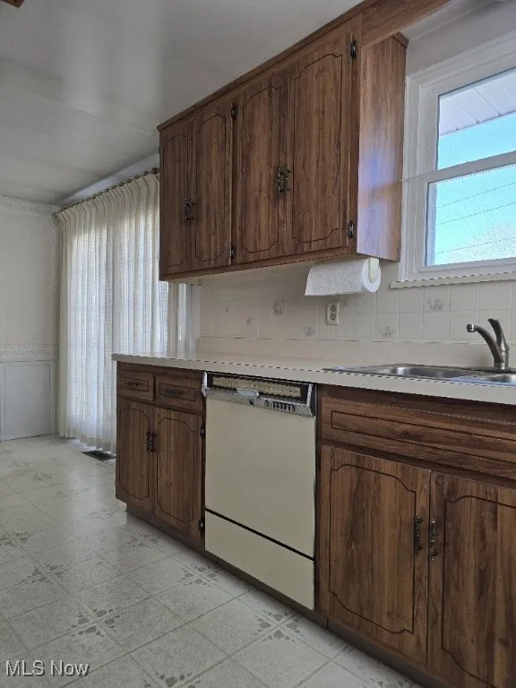 Kitchen featuring light floors, light countertops, white dishwasher, and decorative backsplash.
