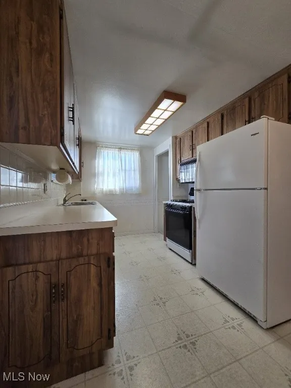 Kitchen featuring light flooring, freestanding refrigerator, light countertops, gas stove, and brown cabinetry