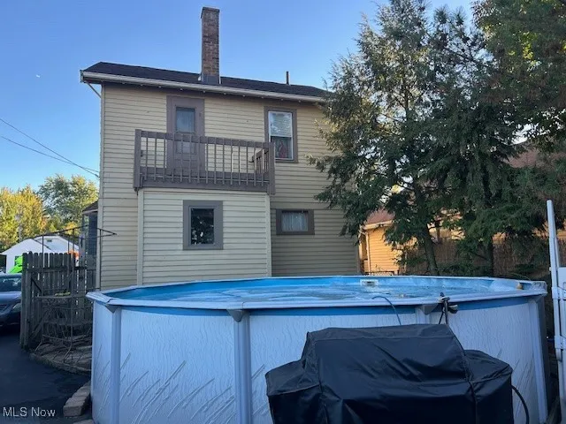 Rear view of property featuring a balcony and outdoor pool