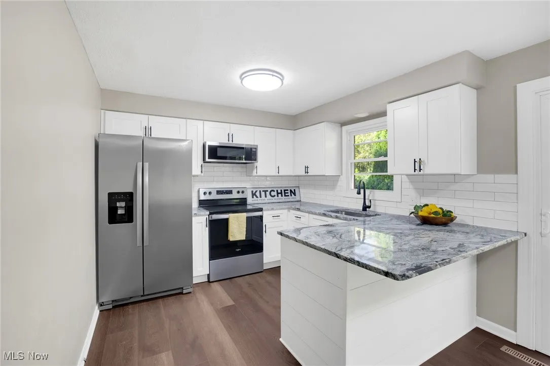 Kitchen featuring stainless steel appliances, light stone counters, white cabinets, and a peninsula