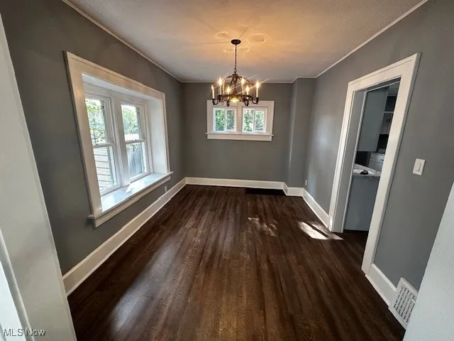 Unfurnished dining area with dark wood finished floors, a chandelier, and crown molding