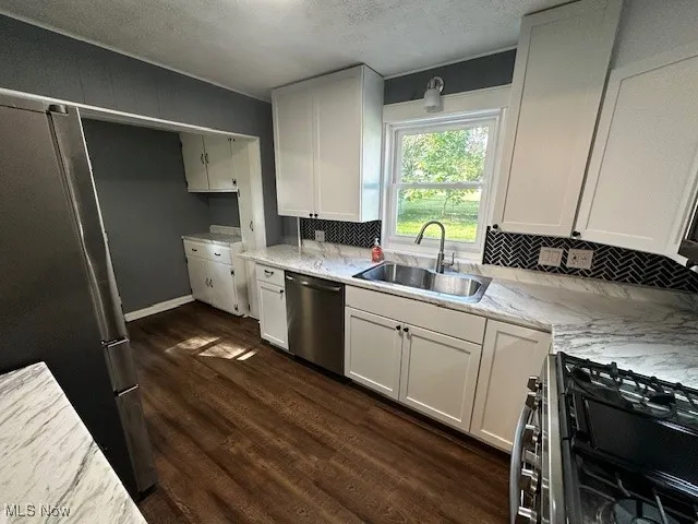 Kitchen with stainless steel appliances, white cabinetry, a textured ceiling, dark wood-style floors, and decorative backsplash