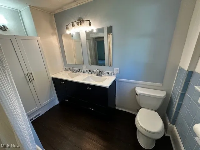 Bathroom with dark wood-style flooring, double vanity, tile walls, and a wainscoted wall