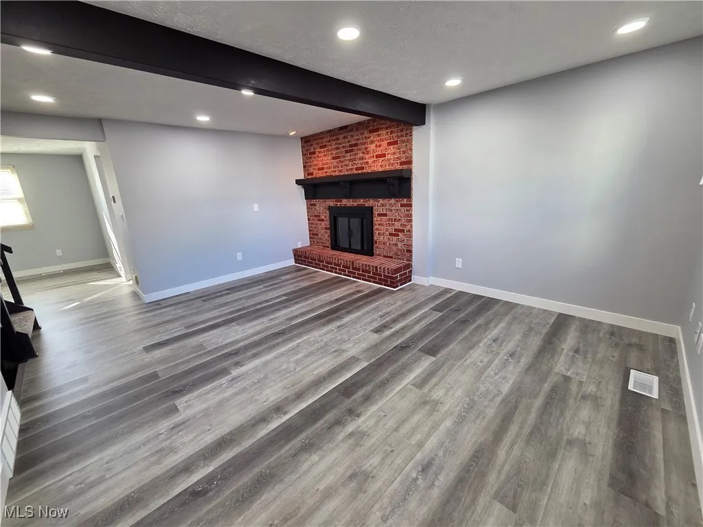 living room featuring beamed ceiling, a textured ceiling, recessed lighting and a brick fireplace