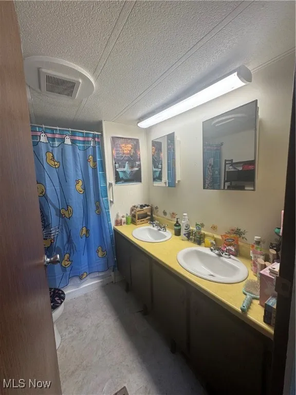 Bathroom with double vanity, a shower with shower curtain, and a textured ceiling