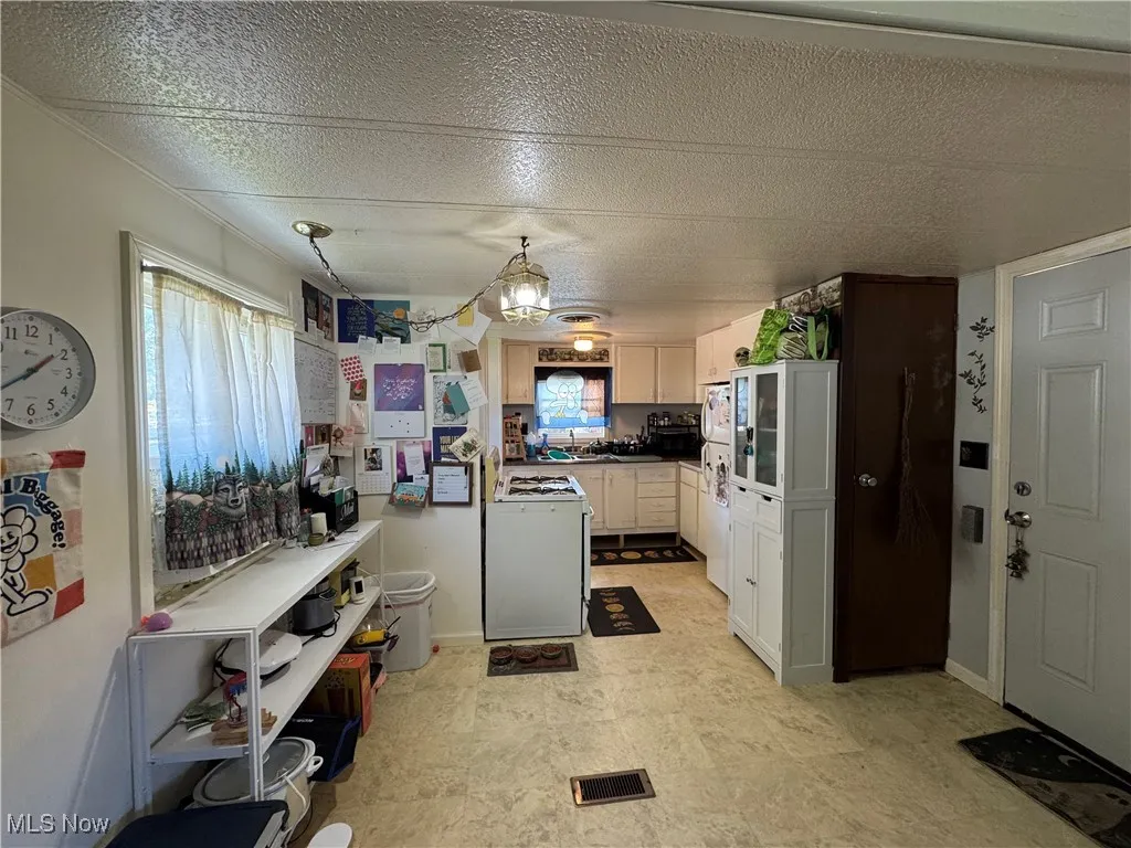 Kitchen with a textured ceiling, white appliances, dark countertops, and white cabinetry
