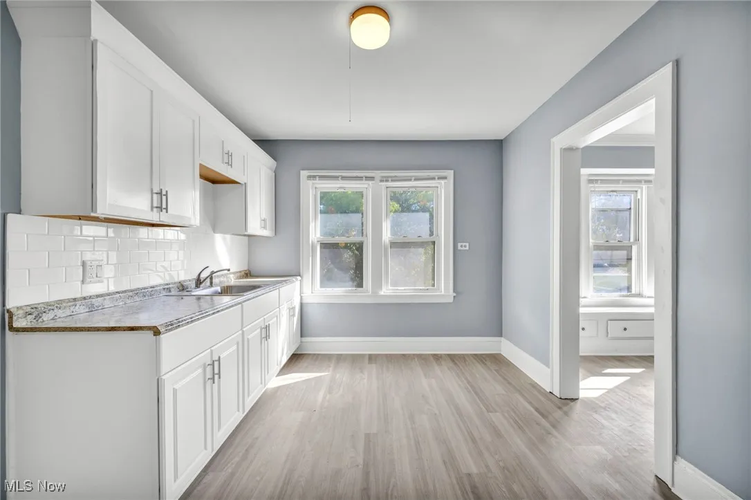 Kitchen with white cabinets, light wood-style floors, backsplash, and light countertops