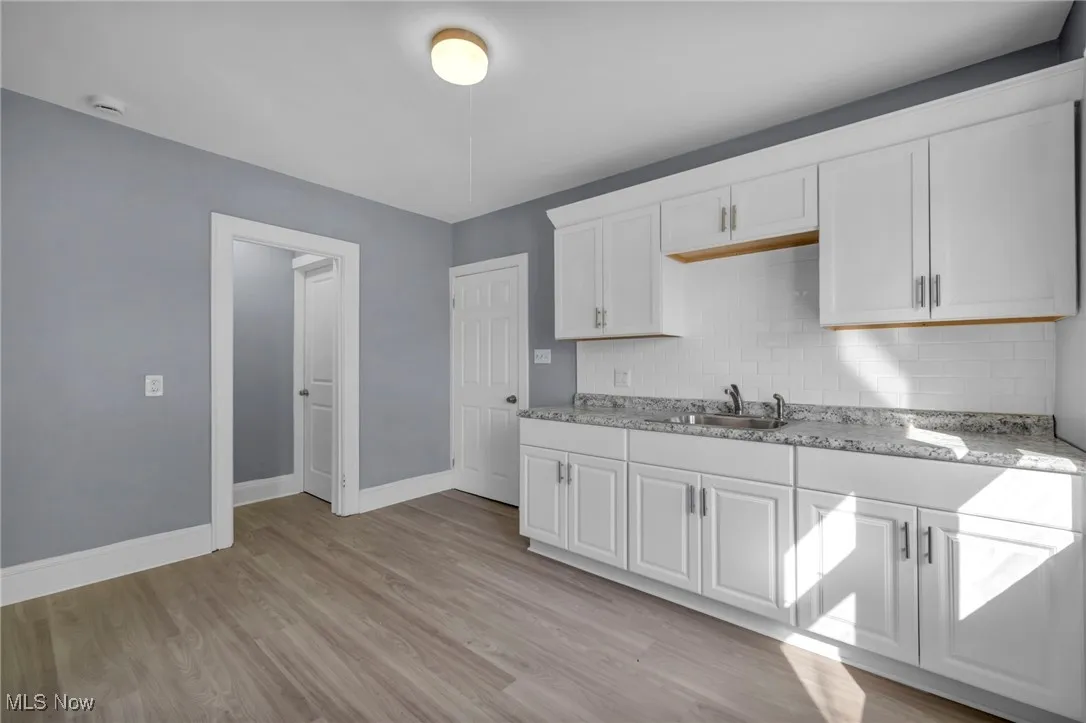 Kitchen with white cabinetry, light wood-style floors, and decorative backsplash