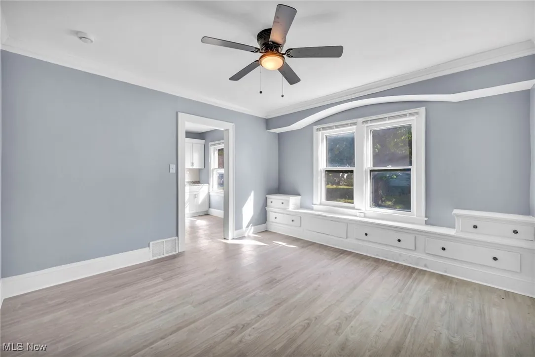 Unfurnished bedroom with light wood-style floors, crown molding, a ceiling fan, and ensuite bath