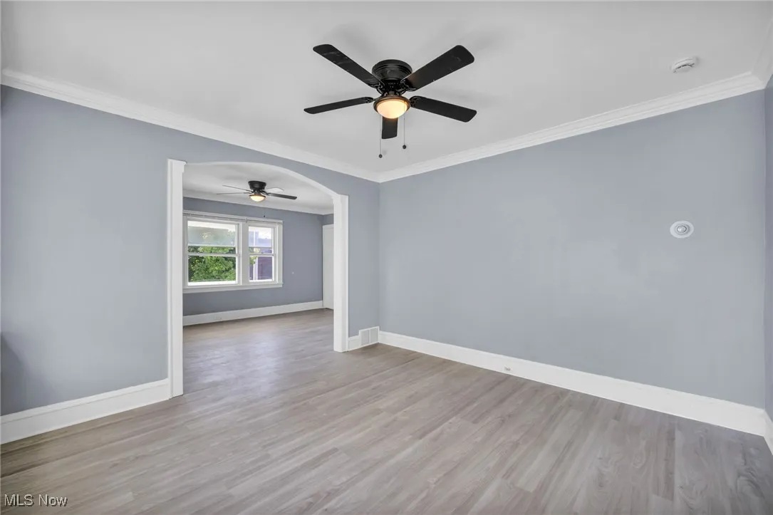 Spare room featuring crown molding, wood finished floors, a ceiling fan, and arched walkways