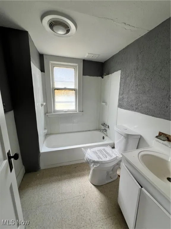 Bathroom with tub / shower combination, vanity, and a textured wall