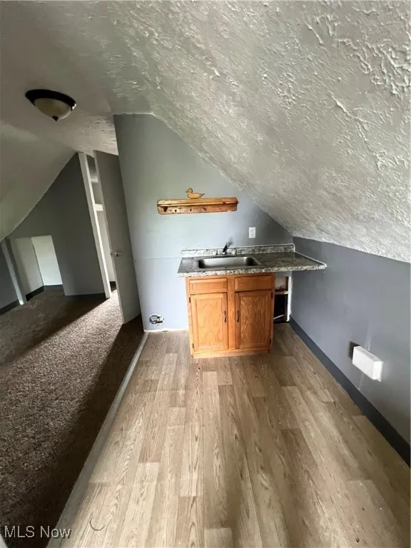 Small kitchen with a textured ceiling, lofted ceiling, light wood-style floors, and brown cabinetry