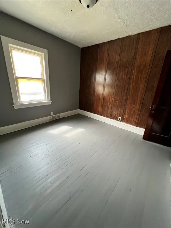bedroom featuring wooden walls, light wood-type flooring, and a textured ceiling