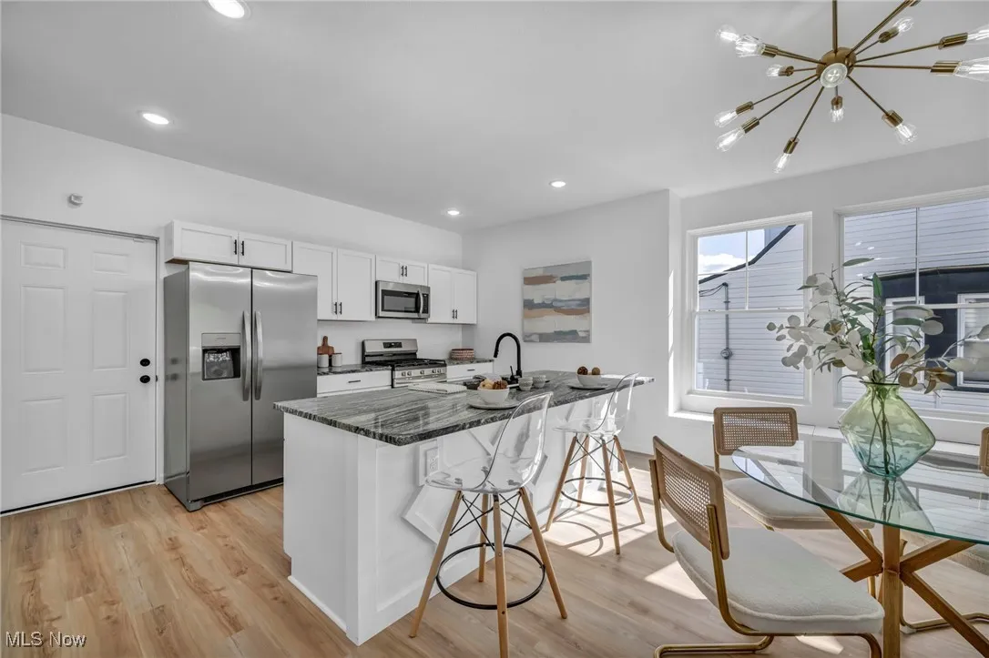 Kitchen with appliances with stainless steel finishes, white cabinets, a kitchen breakfast bar, light wood-style flooring, and dark stone counters