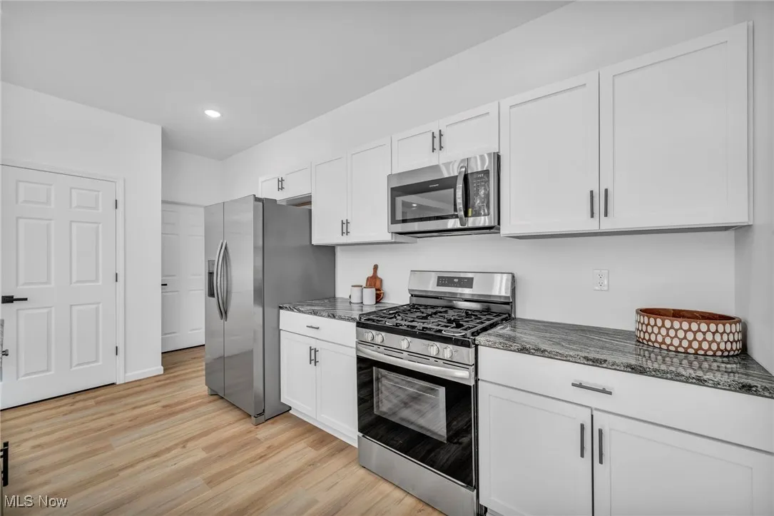 Kitchen featuring stainless steel appliances, white cabinets, dark stone counters, light wood-type flooring, and recessed lighting