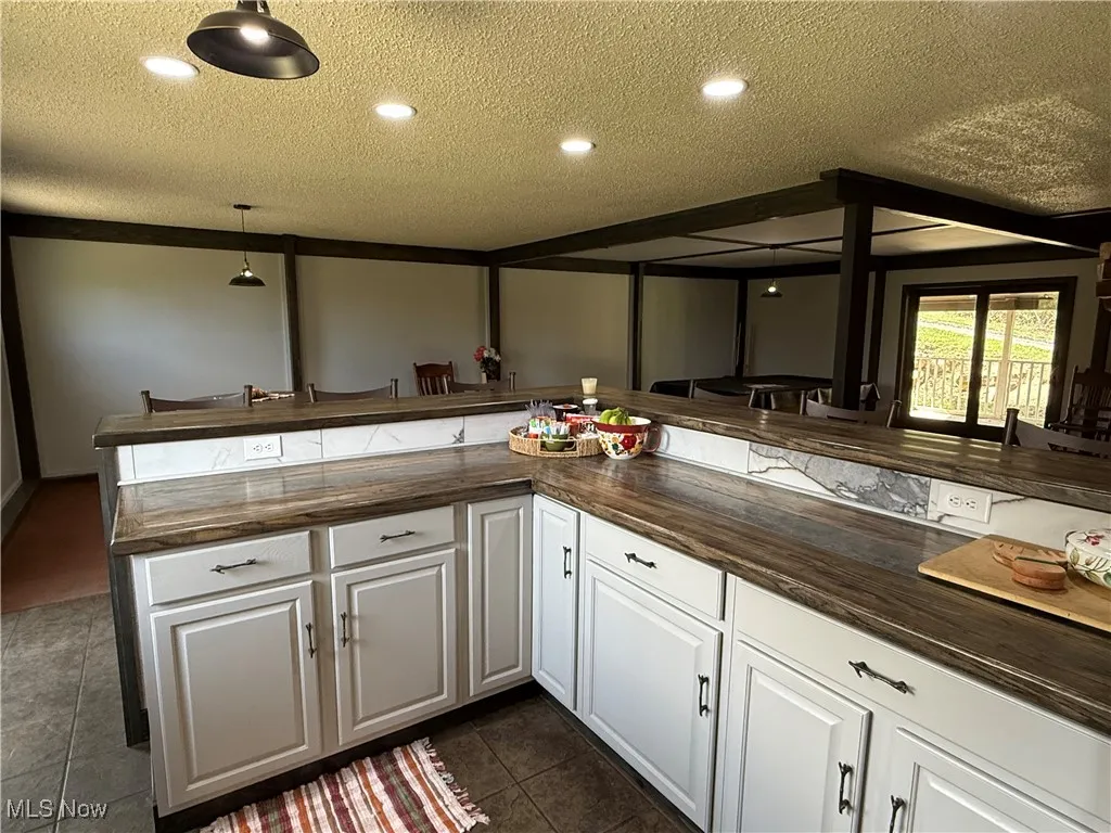 Kitchen featuring white cabinetry, a textured ceiling, hanging light fixtures, dark tile patterned floors, and recessed lighting