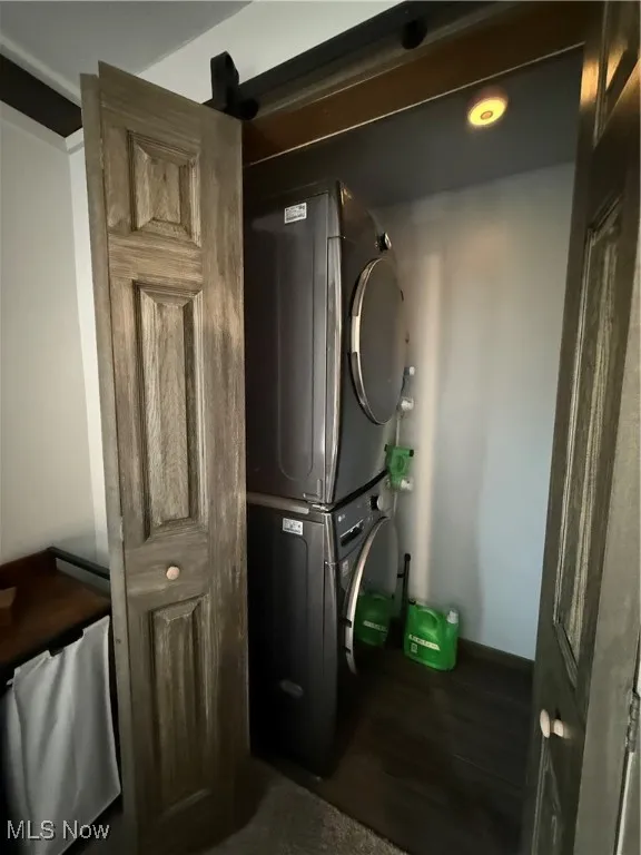 Washroom with dark wood-type flooring and stacked washer / drying machine
