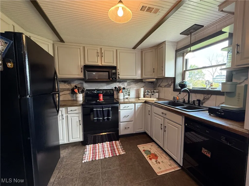 Kitchen featuring black appliances, tasteful backsplash, dark tile patterned floors, and pendant lighting