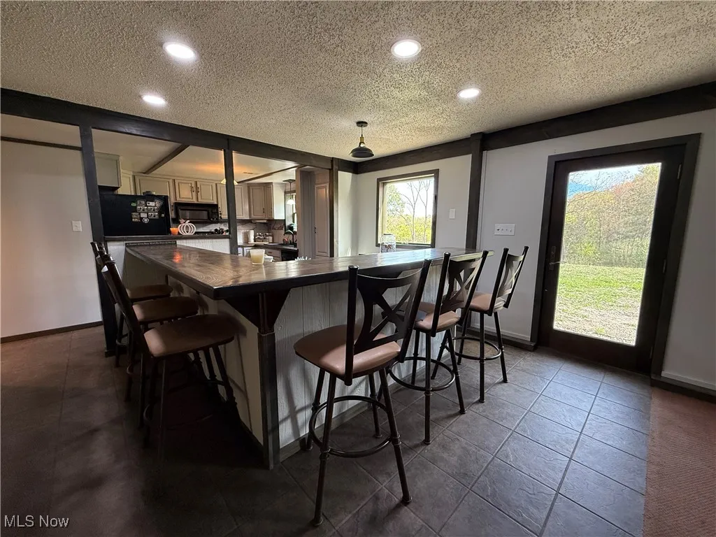 Kitchen with dark countertops, a kitchen breakfast bar, a textured ceiling, recessed lighting, and black appliances