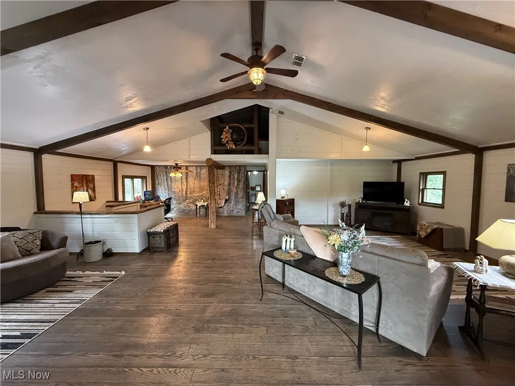 Living room featuring healthy amount of natural light, a ceiling fan, dark wood-style floors, and wood walls