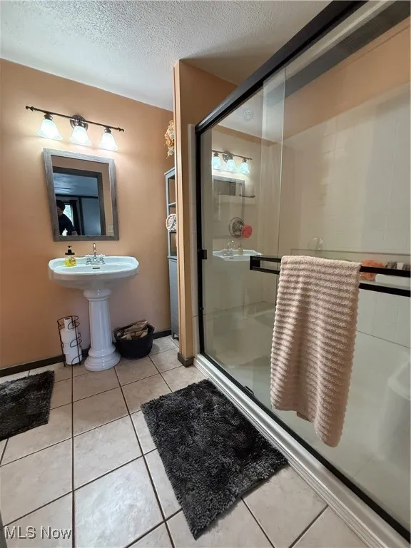 Bathroom with a stall shower, a textured ceiling, and light tile patterned floors