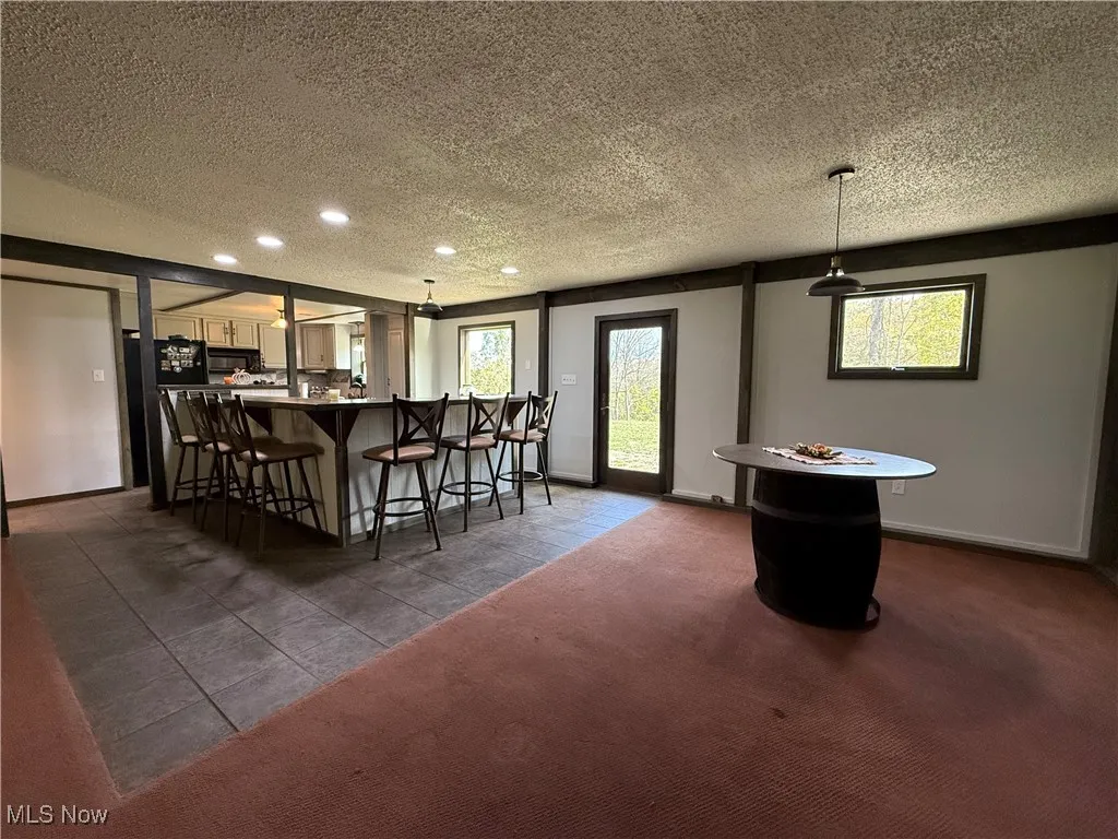 Indoor bar featuring a textured ceiling, hanging light fixtures, freestanding refrigerator, dark tile patterned flooring, and recessed lighting