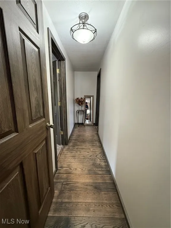 Corridor with dark wood-type flooring and baseboards