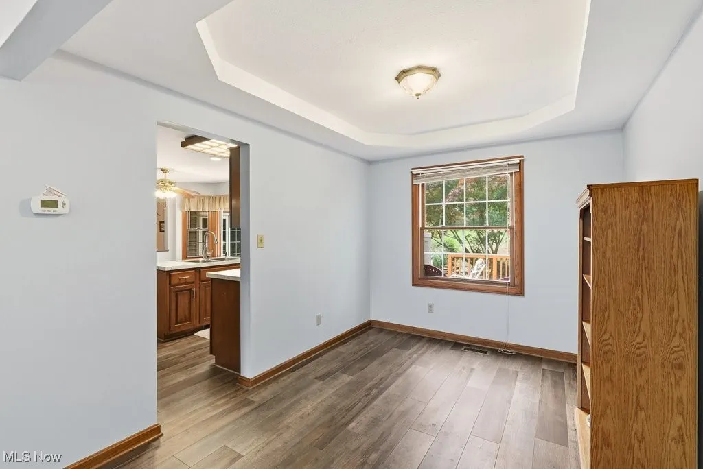 Dining room with a raised ceiling, dark wood-style floors, and a ceiling fan