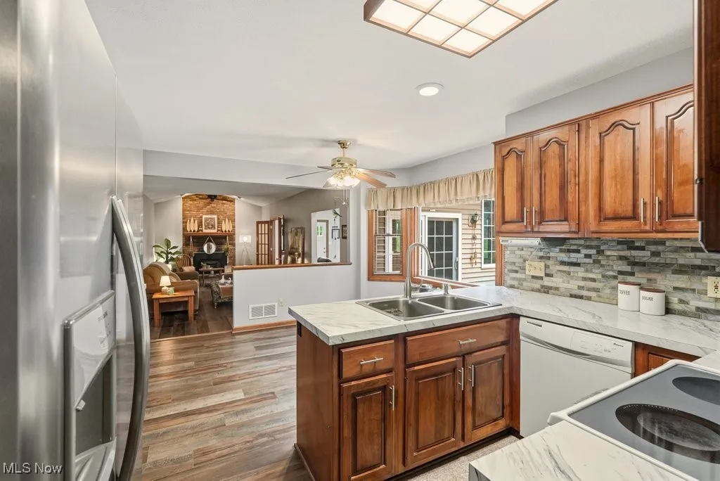 Kitchen with stainless steel fridge with ice dispenser, white dishwasher, light countertops, brown cabinets, and light wood-type flooring