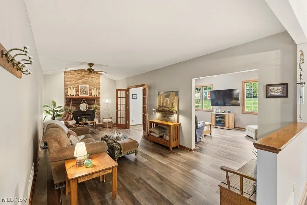 Living area featuring wood finished floors, lofted ceiling, a brick fireplace, and a ceiling fan
