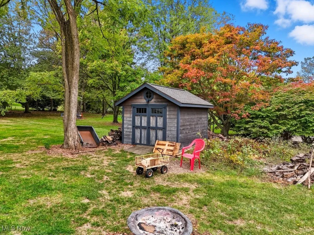 View of grassy yard featuring view of scattered trees, an outdoor fire pit, and a storage shed