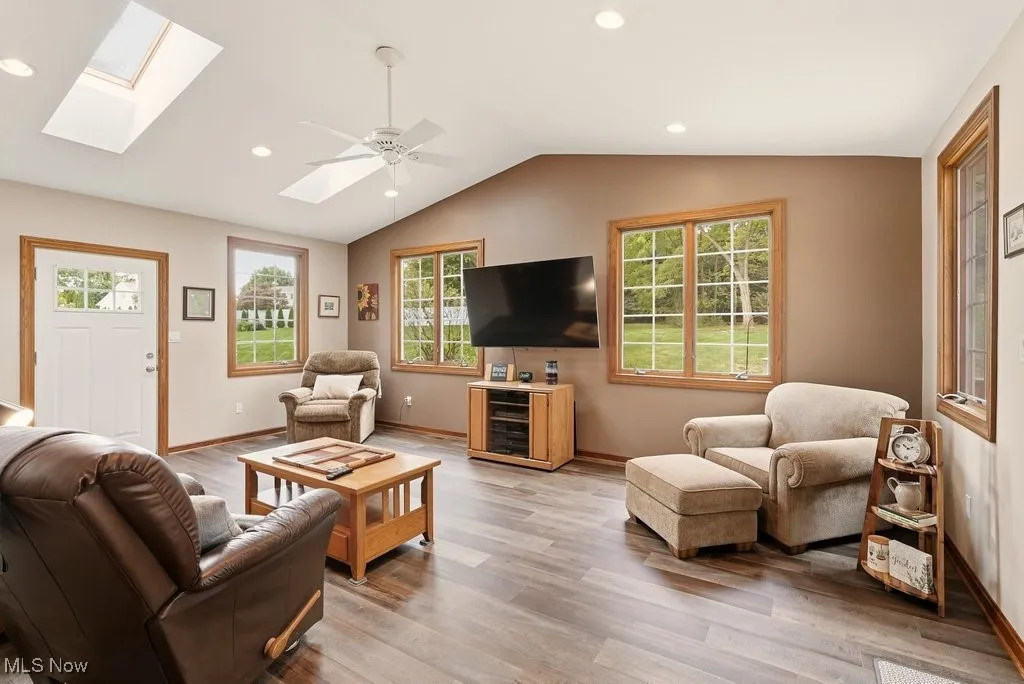Living area with vaulted ceiling, light wood-style flooring, a skylight, recessed lighting, and a ceiling fan