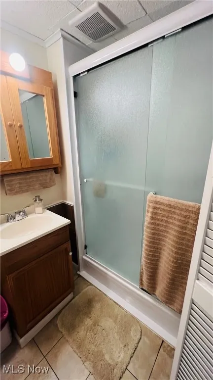 Bathroom featuring a shower stall, vanity, light tile flooring
