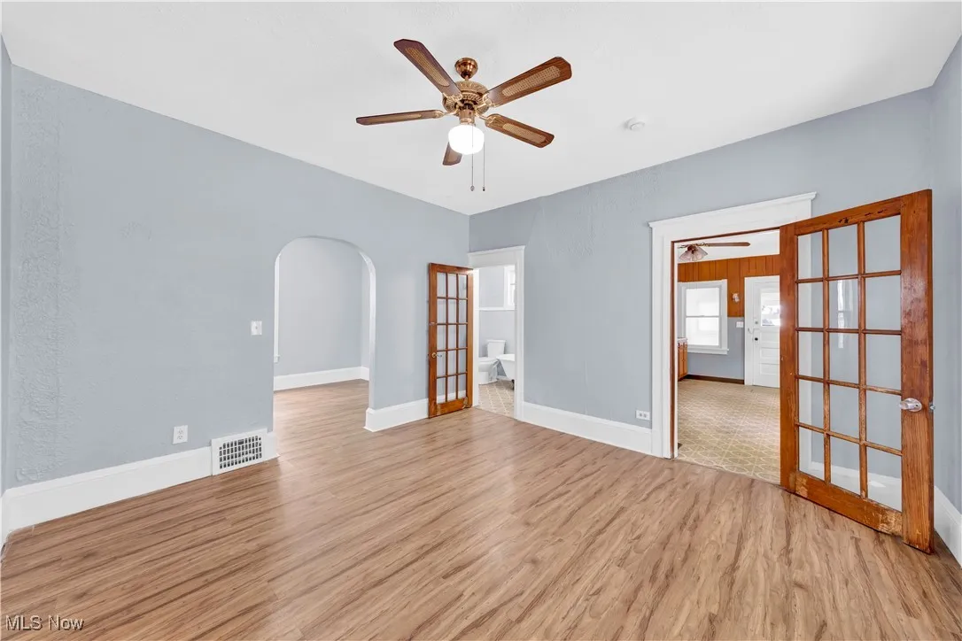 Spare room with light wood-style floors, arched walkways, french doors, and a ceiling fan