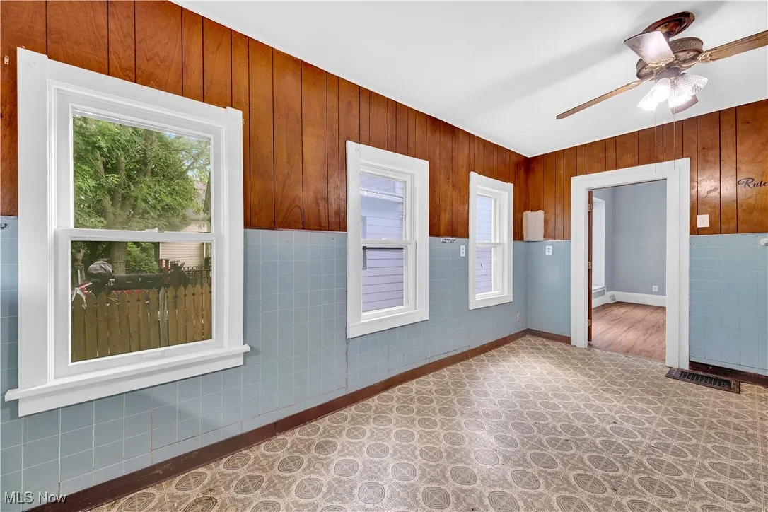 Unfurnished room with a wainscoted wall, plenty of natural light, wooden walls, ceiling fan, and tile walls