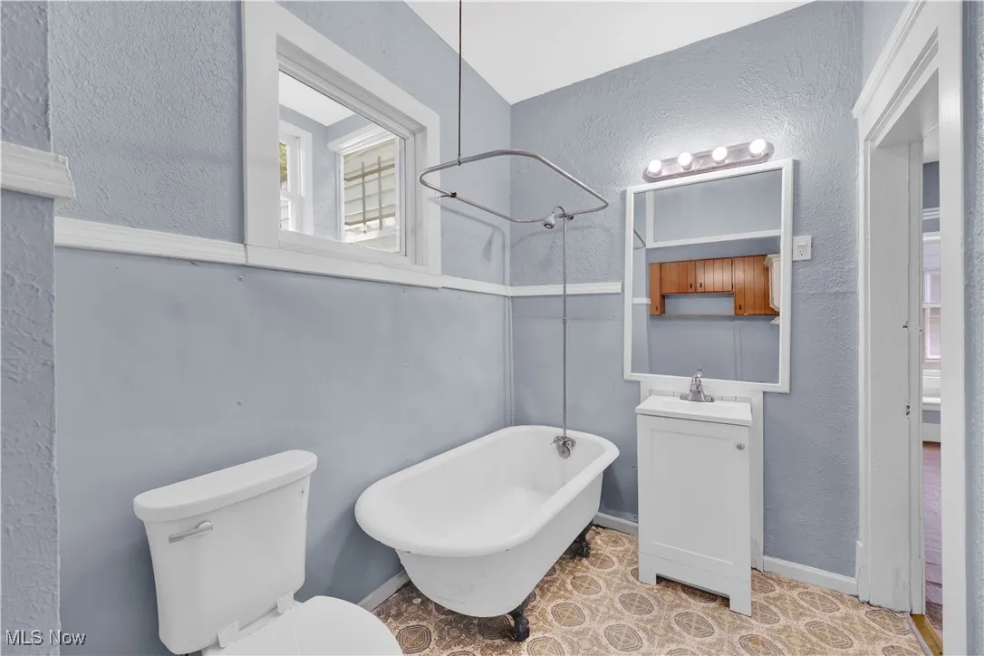 Full bath with a textured wall, vanity, and a combined bath / shower with freestanding tub