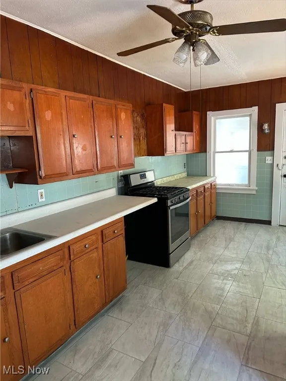 Kitchen featuring brown cabinetry, stainless steel range with gas cooktop, light countertops, a ceiling fan, and a textured ceiling