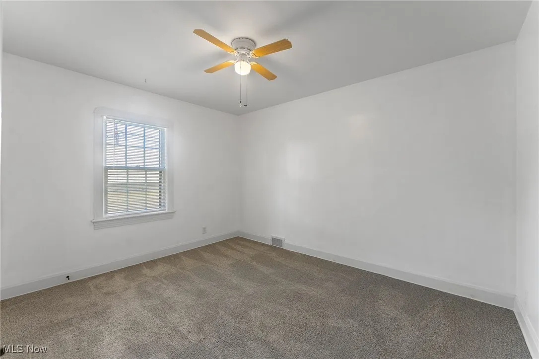 Carpeted spare room with ceiling fan and baseboards