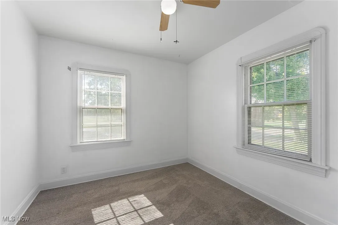 Unfurnished room with dark colored carpet and a ceiling fan