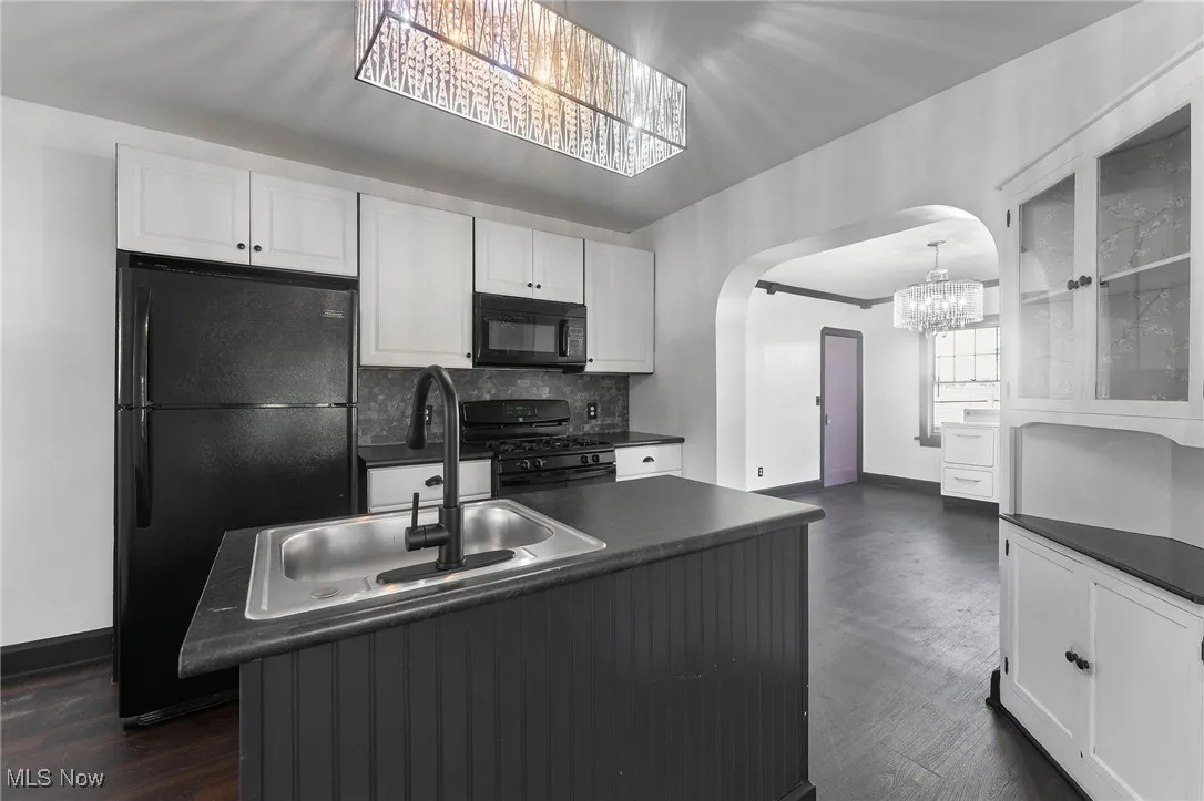 Kitchen featuring arched walkways, dark countertops, black appliances, and white cabinets