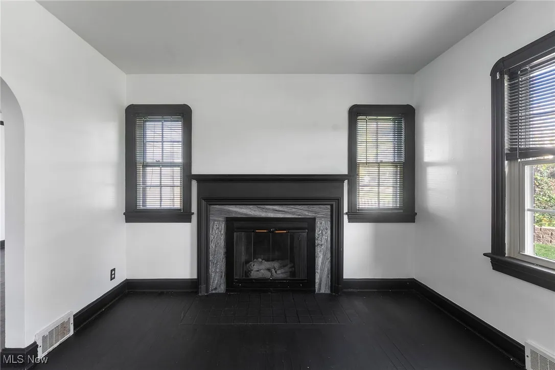 Unfurnished living room with a glass covered fireplace, arched walkways, and dark wood-style flooring