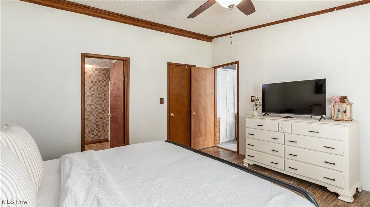 Bedroom with ensuite bath, ornamental molding, a textured ceiling, wood finished floors, and ceiling fan