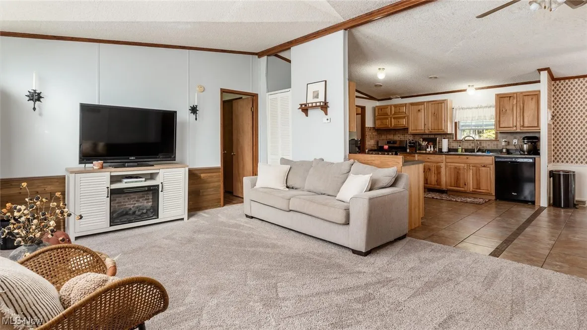 Living room featuring light tile patterned floors, a textured ceiling, ornamental molding, a ceiling fan, and light colored carpet