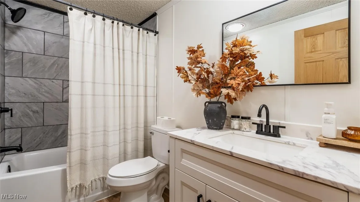 Bathroom featuring a textured ceiling, shower / tub combo with curtain, and vanity