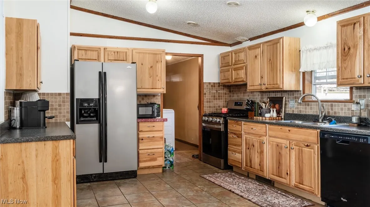 Kitchen featuring a textured ceiling, black appliances, dark countertops, decorative backsplash, and light tile patterned flooring