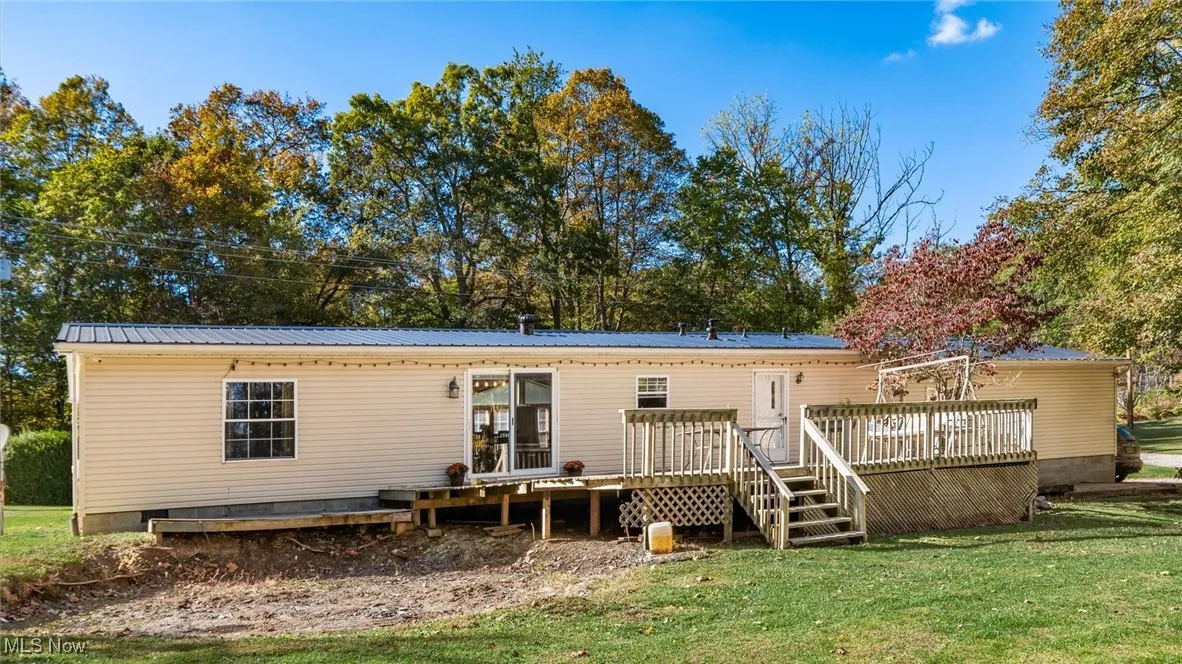 Back of property with a metal roof, a deck, crawl space, a lawn, and view of scattered trees
